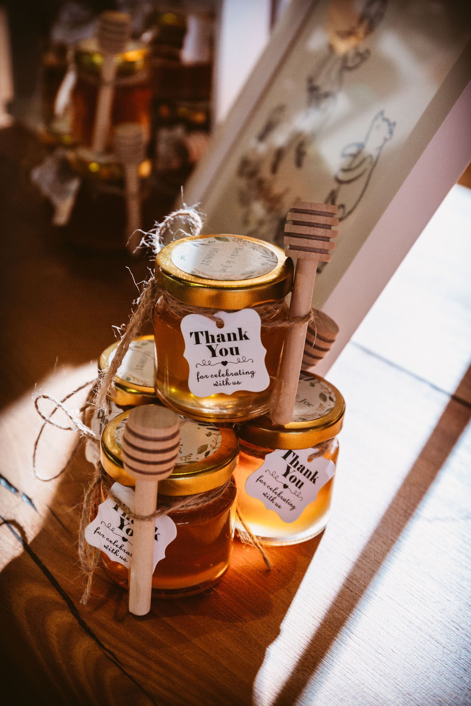 Honey jars with 'Thank You' tags arranged as wedding favors on wooden surface.