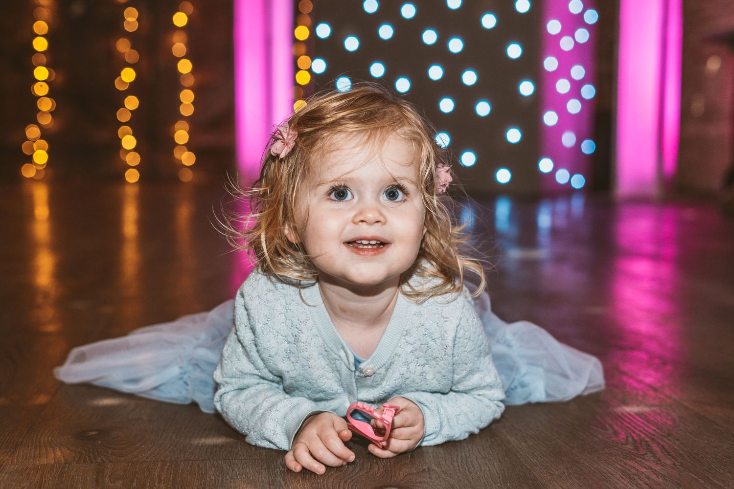 Small child lying on floor with colorful bokeh lights in background.