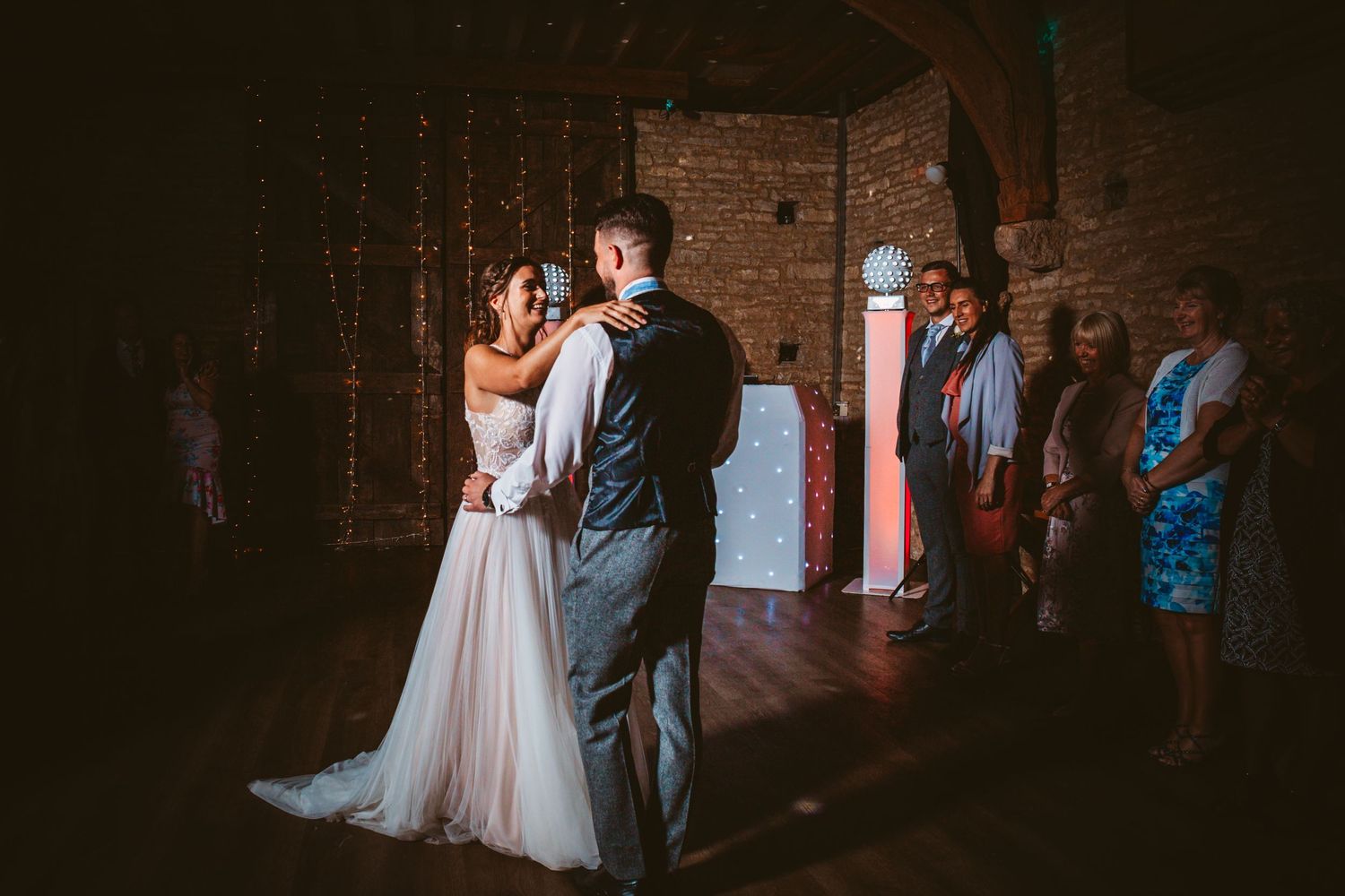 Tender dance moment in dimly lit brick-walled reception venue.