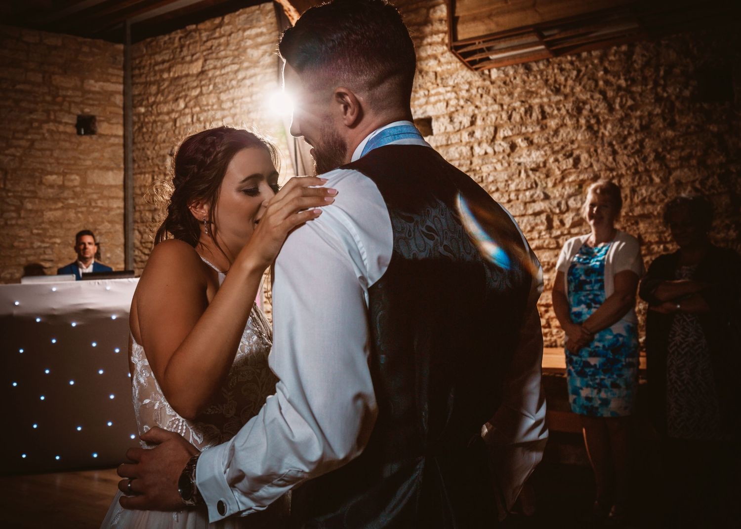 Couple shares romantic dance moment in rustic brick venue with fairy lights.