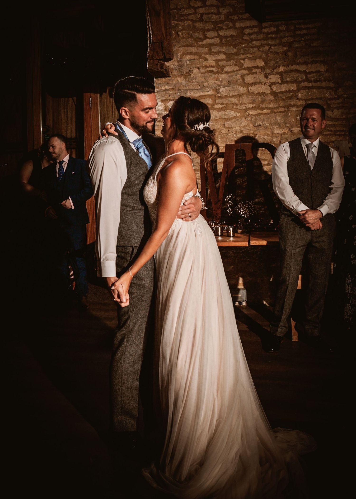 A romantic first dance at a rustic brick-walled wedding venue with the couple embracing in soft lighting.