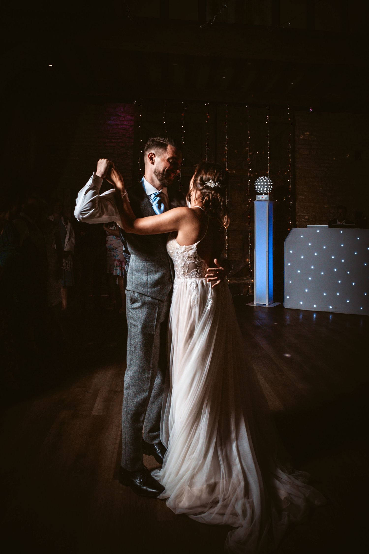 Intimate slow dance moment beneath twinkling string lights at wedding reception.