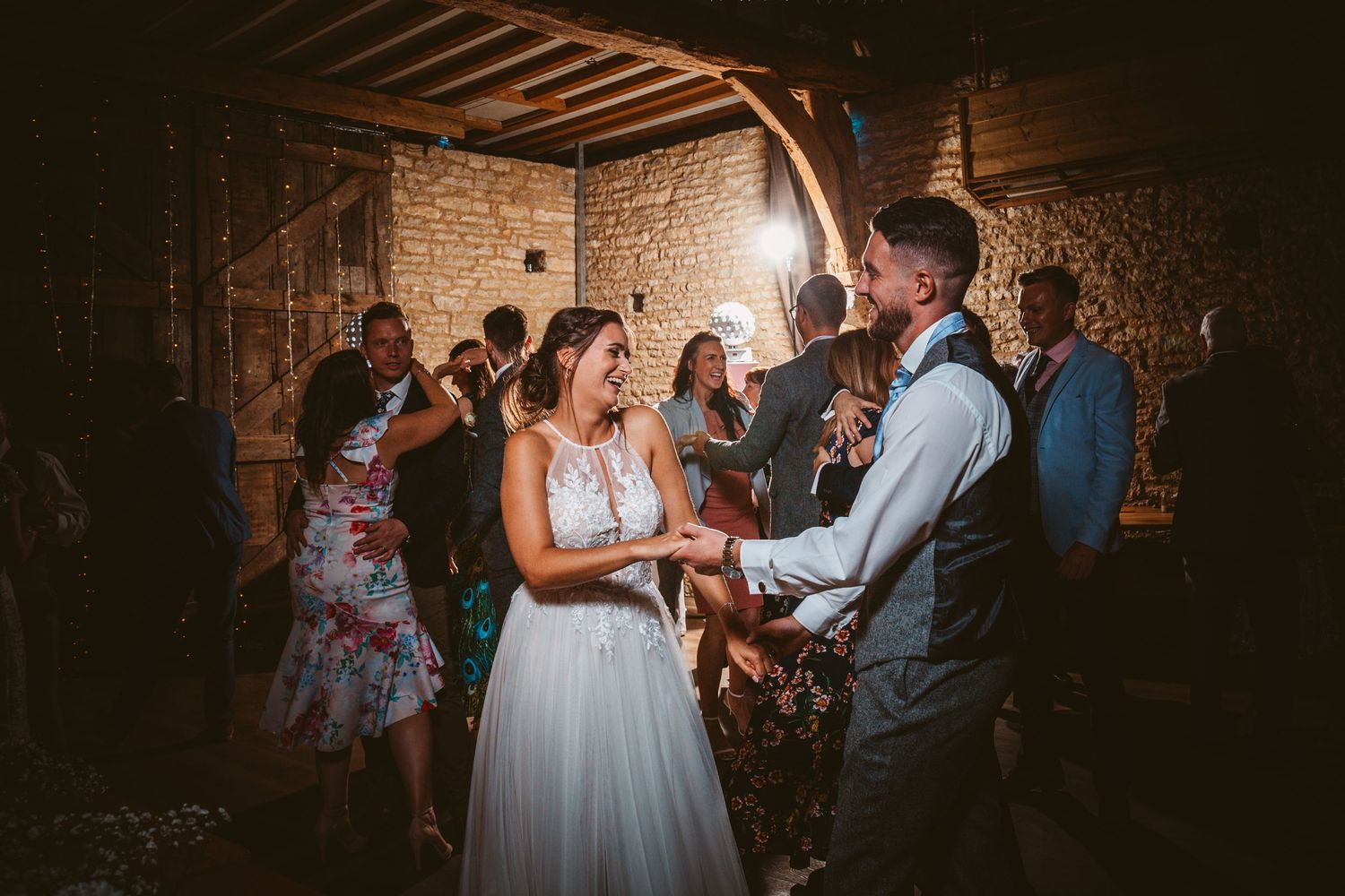 Wedding guests dancing and celebrating in a rustic indoor venue with stone walls and warm lighting.