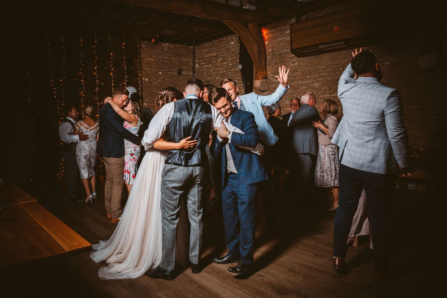 Wedding celebration dance party in industrial brick venue with string lights.