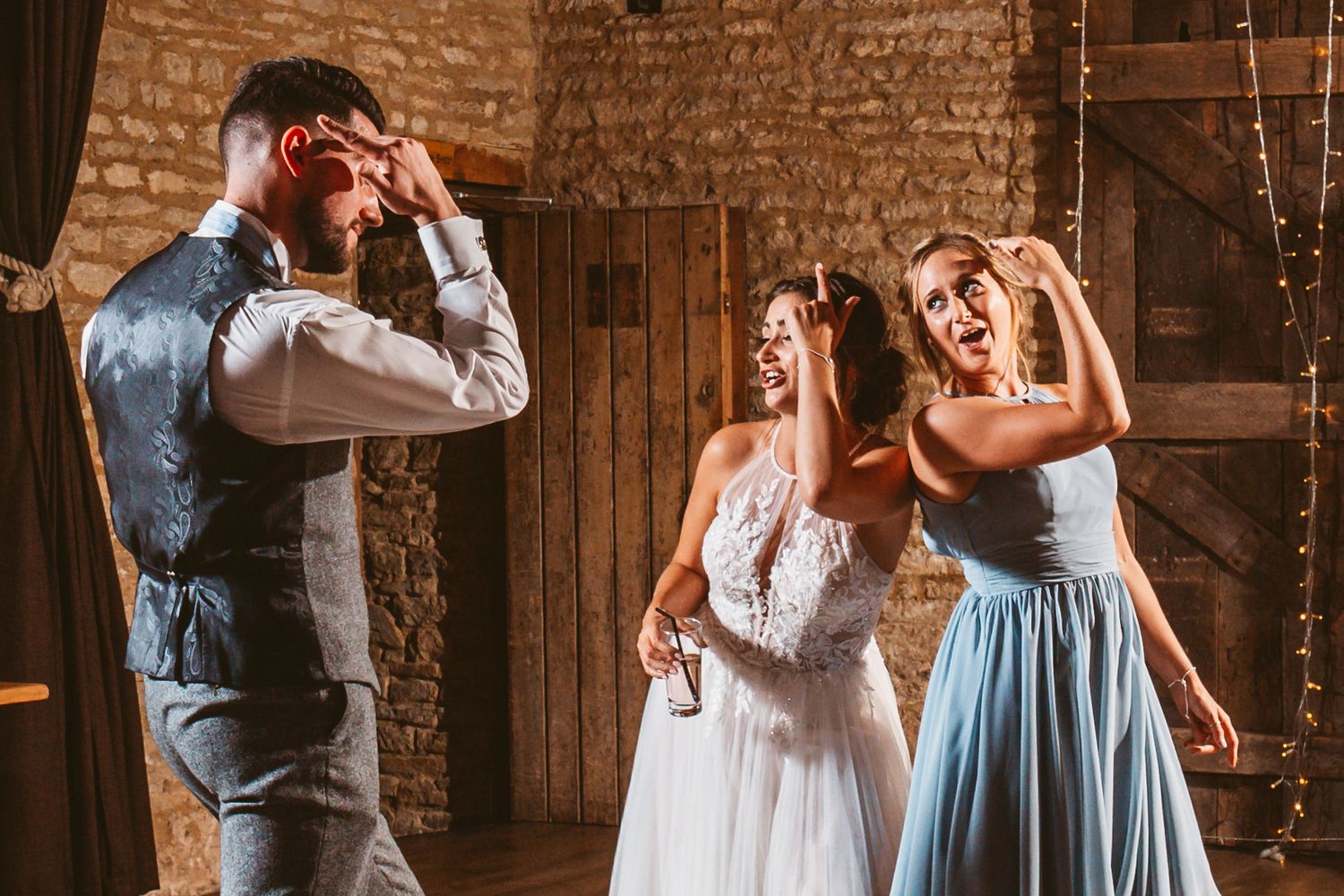 Wedding party members posing playfully inside a rustic barn venue.