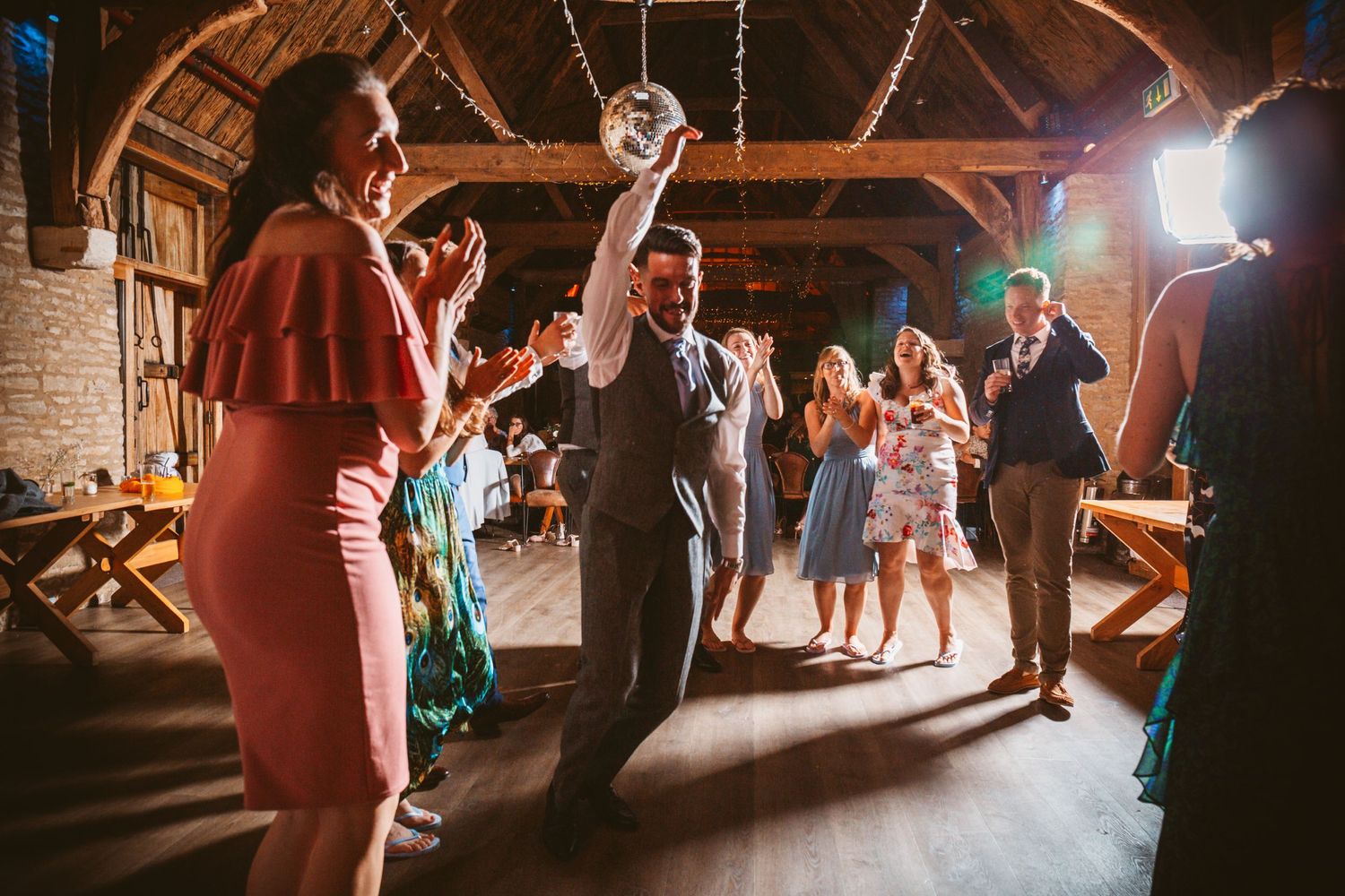 Wedding reception dance party in a rustic barn venue with disco ball and wooden beams.