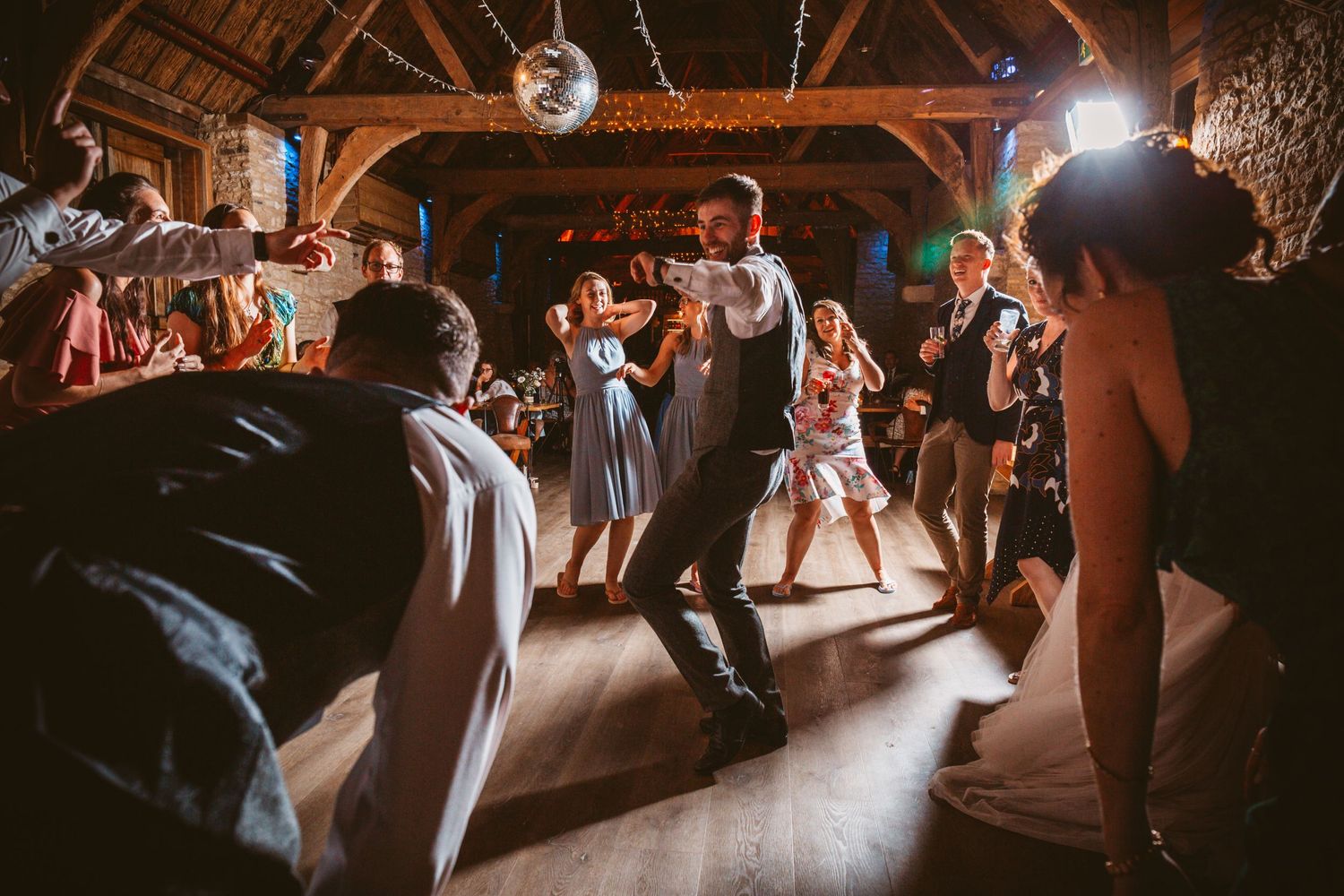 Lively dance party at a rustic barn wedding reception with dramatic lighting.