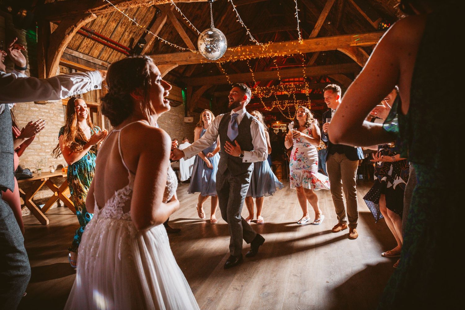 Wedding guests dancing and celebrating on a wooden dance floor in a rustic barn venue.