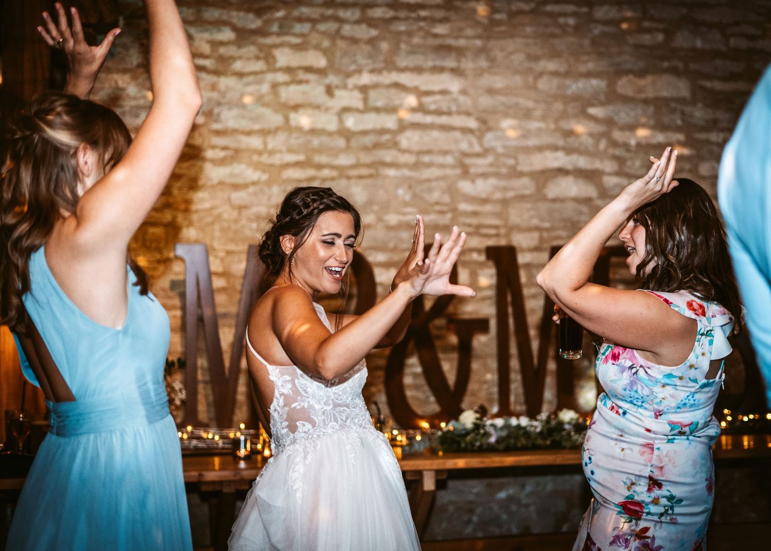 Guests dancing energetically at a rustic barn wedding reception with exposed brick walls.