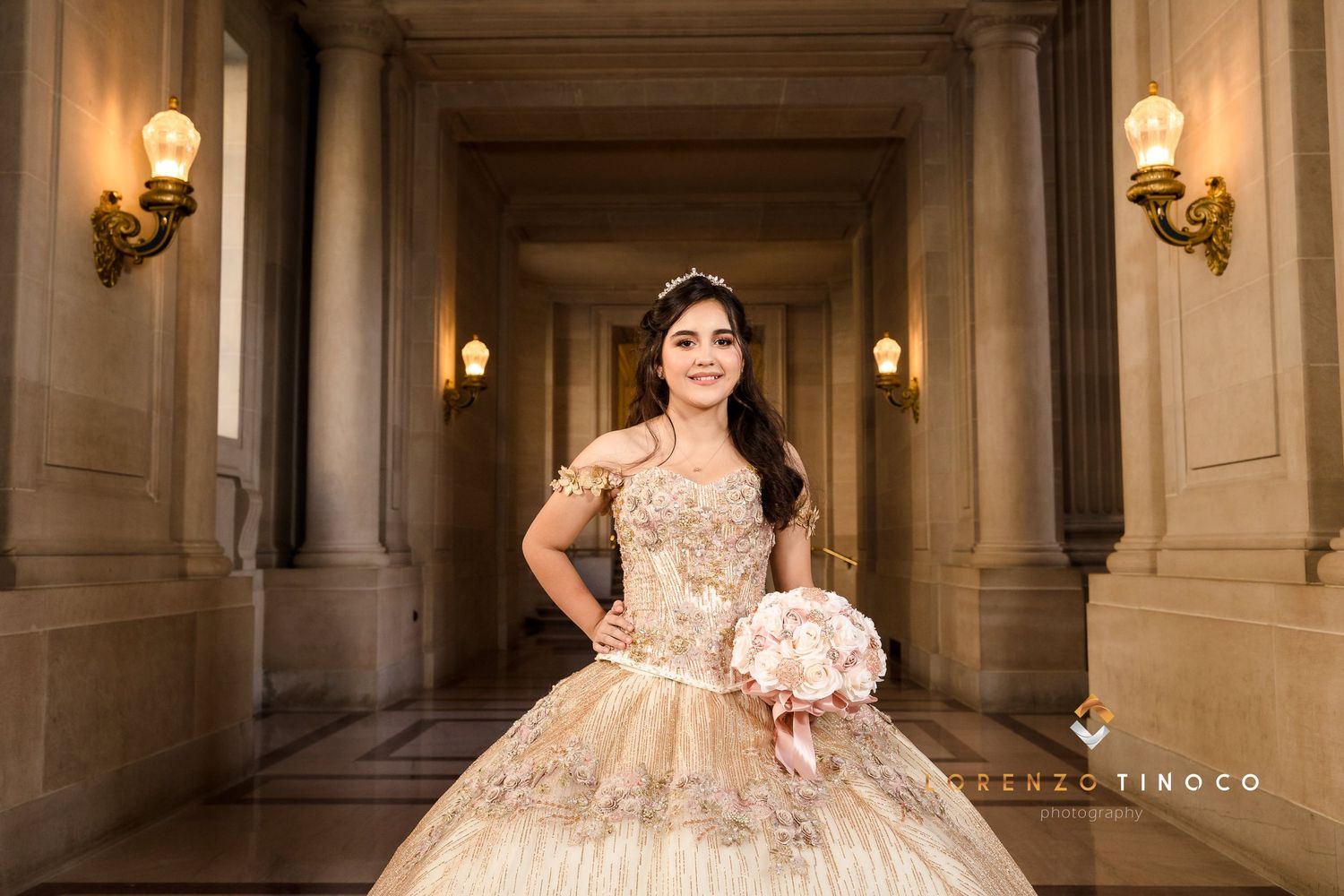 A stunning champagne-colored ball gown with intricate beading is showcased in an elegant hallway with wall sconces.
