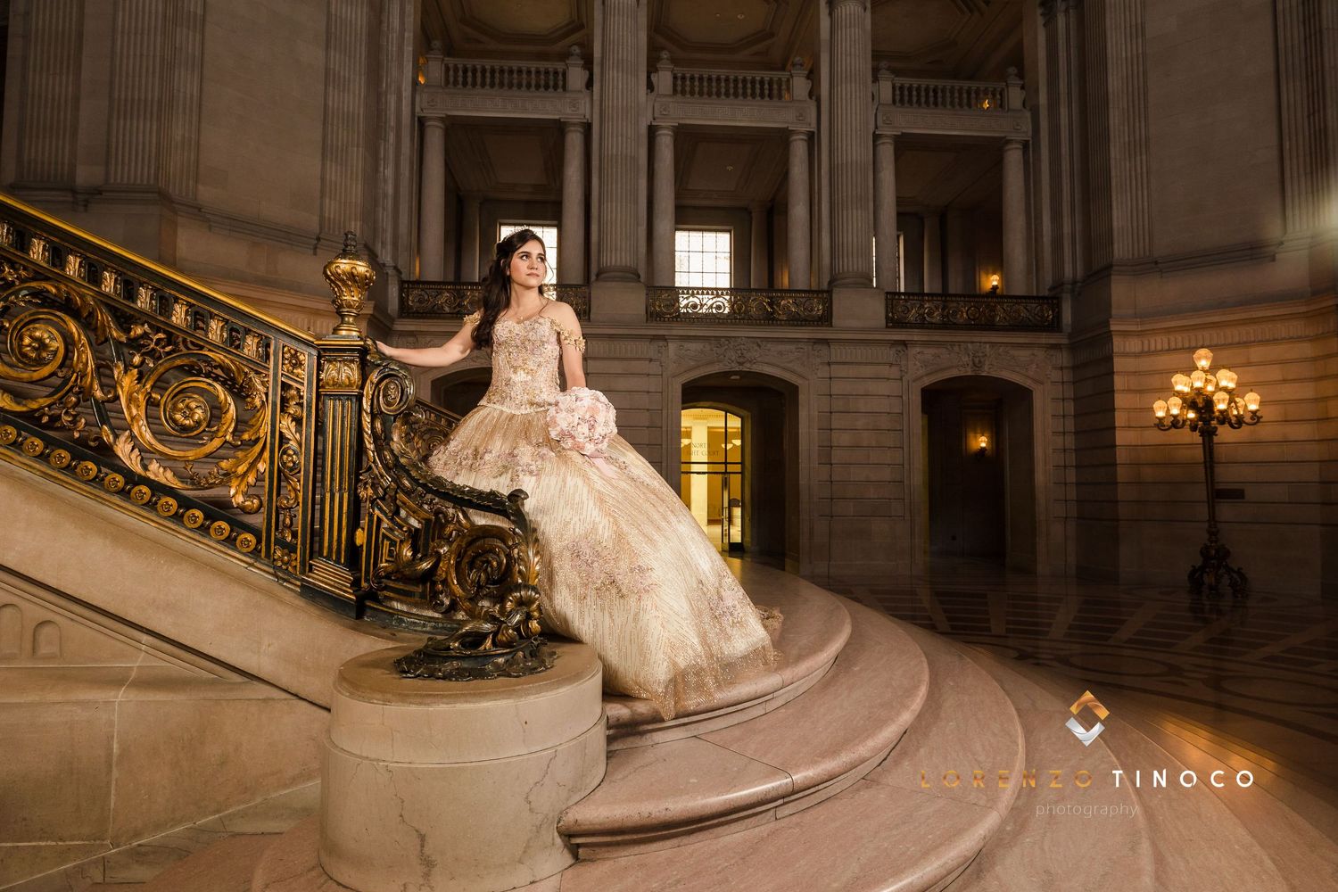 A glamorous gold ballgown sparkles on the grand marble staircase of an opulent historic building.