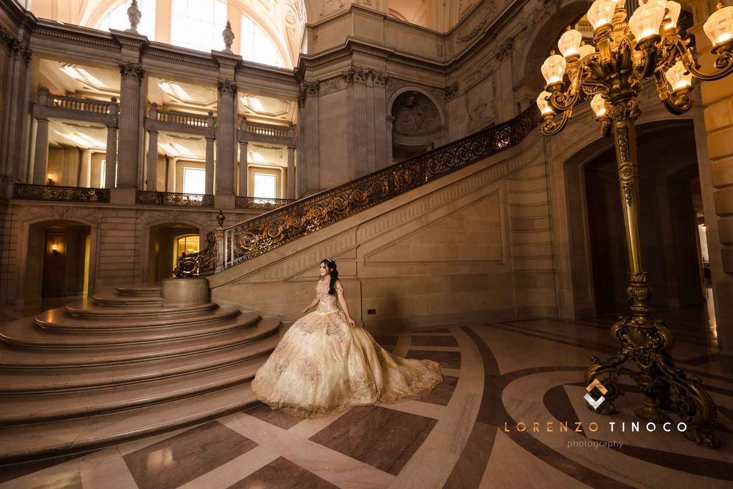 A flowing champagne ballgown creates drama against the architectural grandeur of a historic staircase.