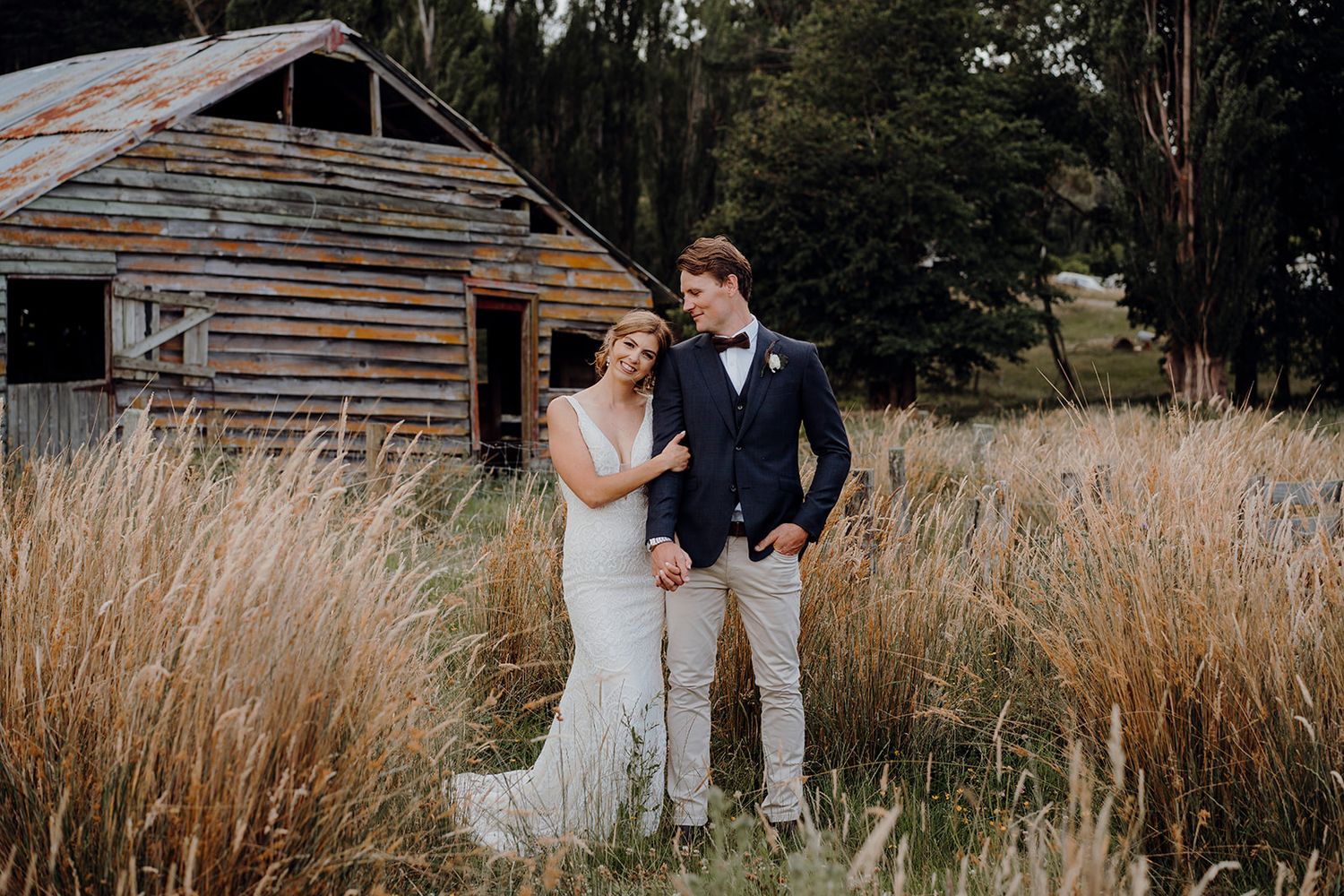 bride and groom posing in front of a wooden barn
