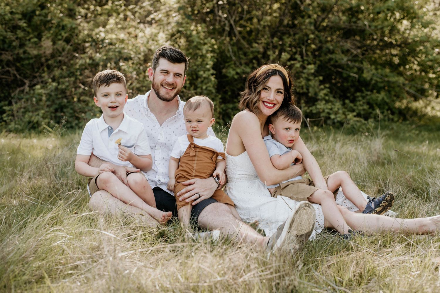 Family of five sitting together on grassy hill during outdoor portrait session.
