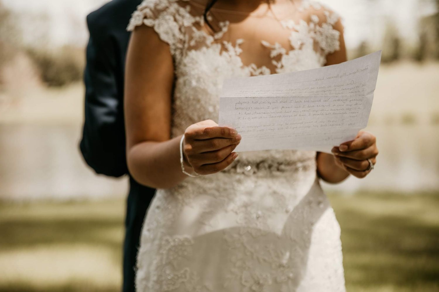 Close-up of hands holding handwritten vows in a delicate lace wedding dress.