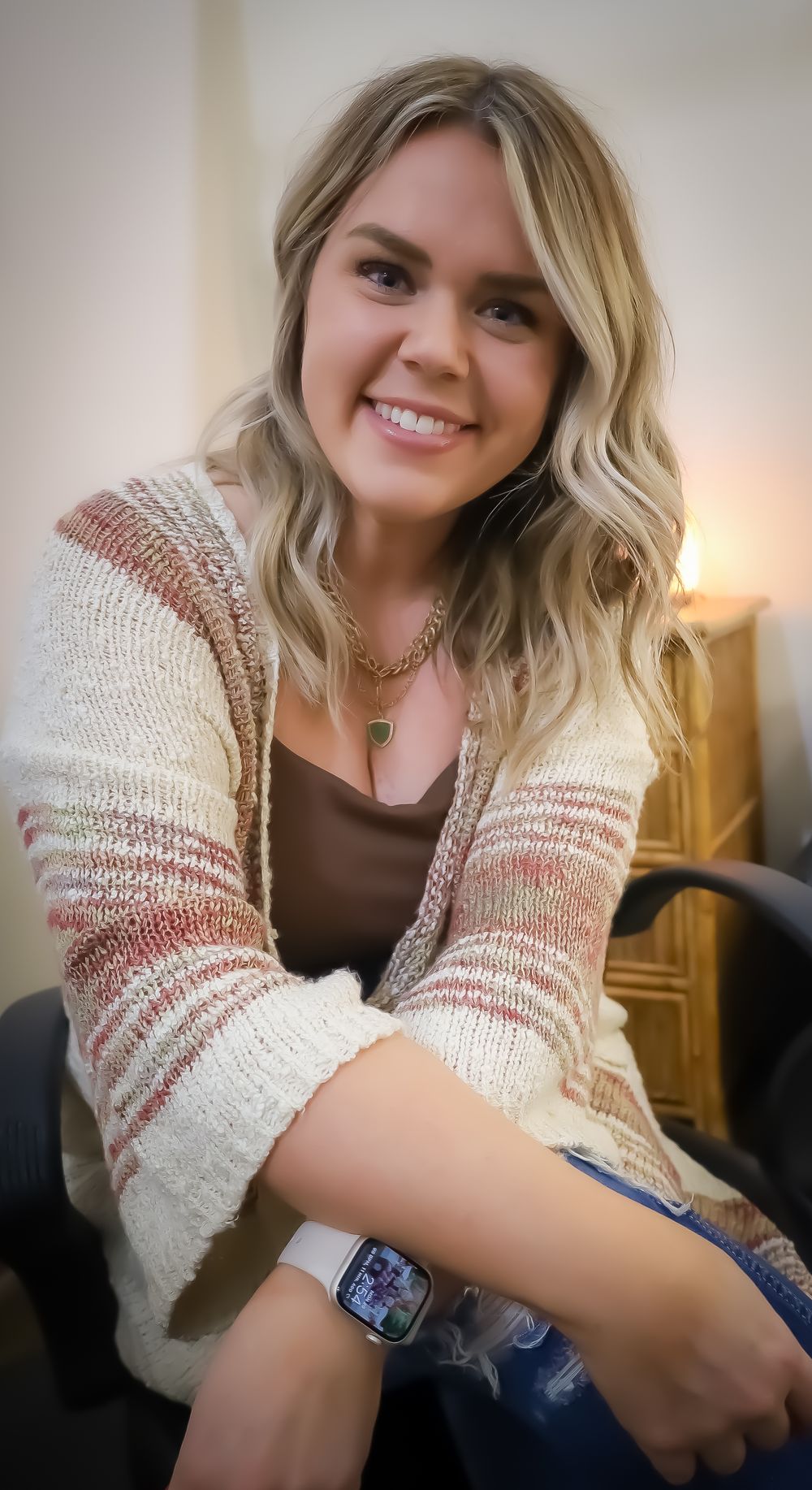 Casual portrait in striped cardigan and smart watch against warm indoor lighting.