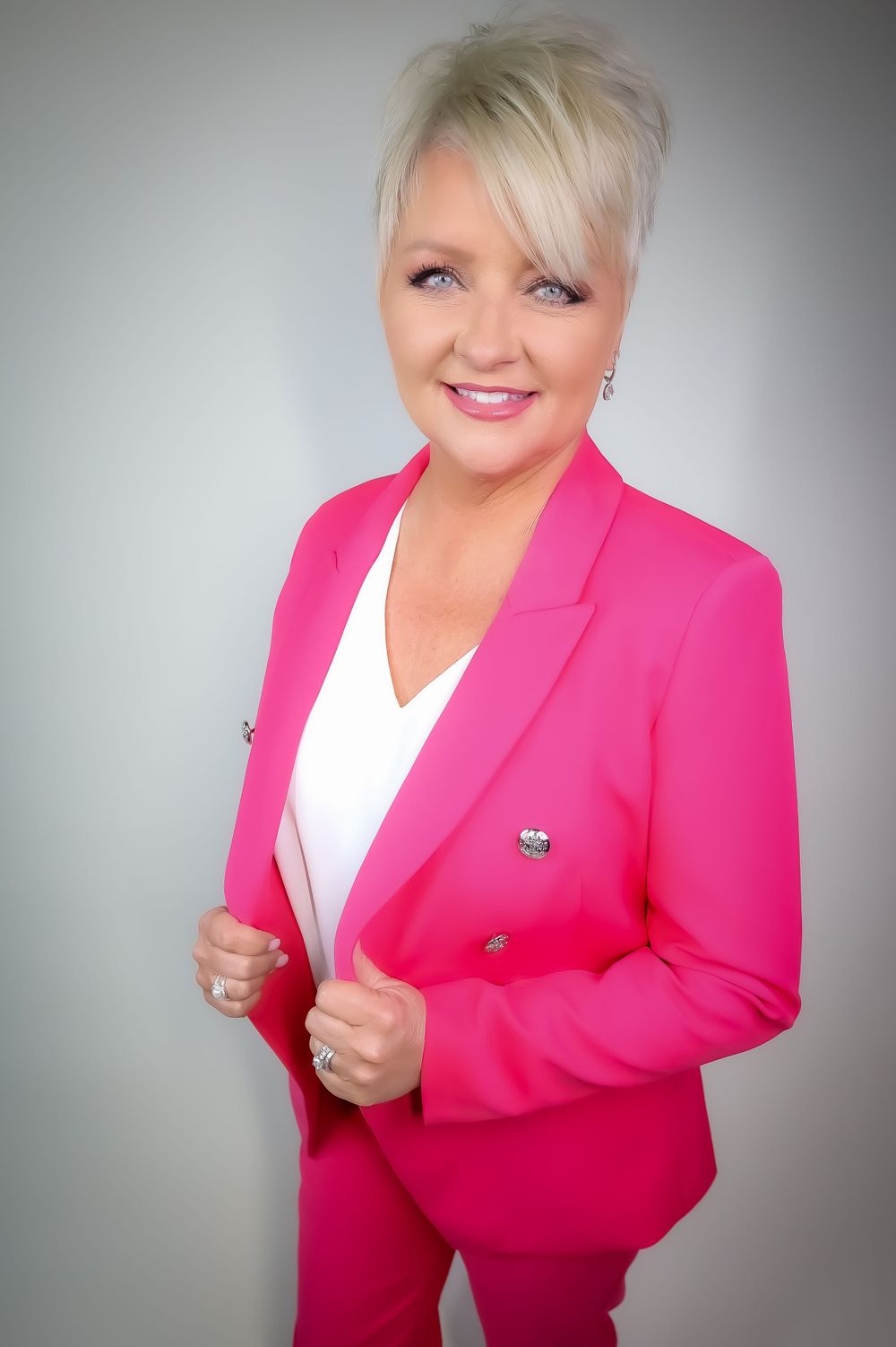 Professional headshot in bright pink blazer and white blouse against light grey background.