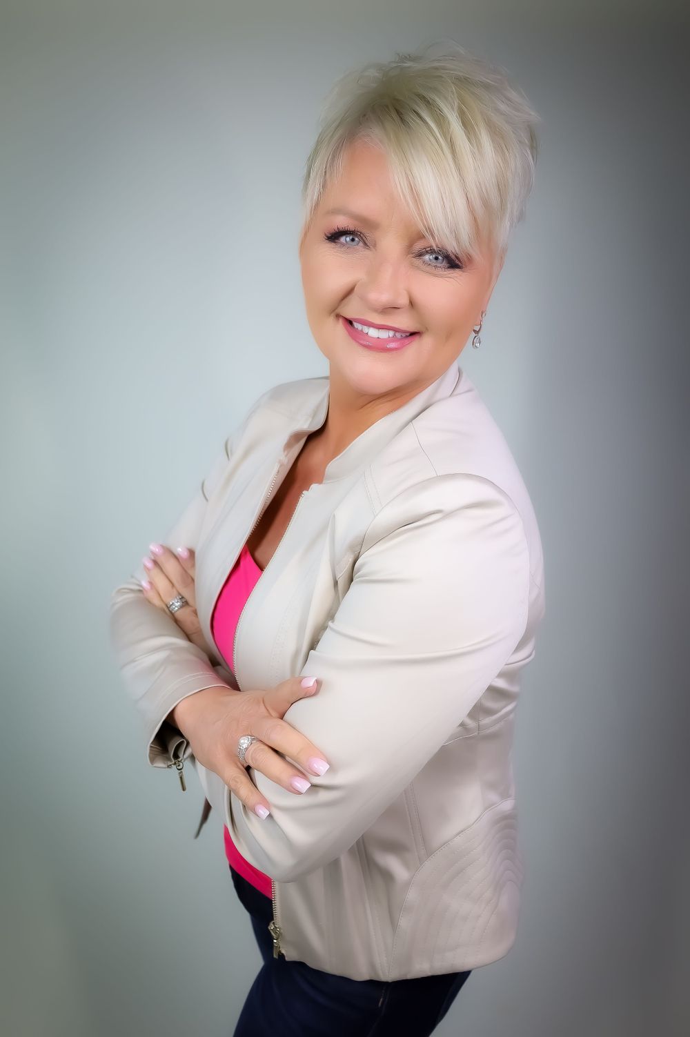 Professional portrait against grey background wearing cream blazer and pink top.