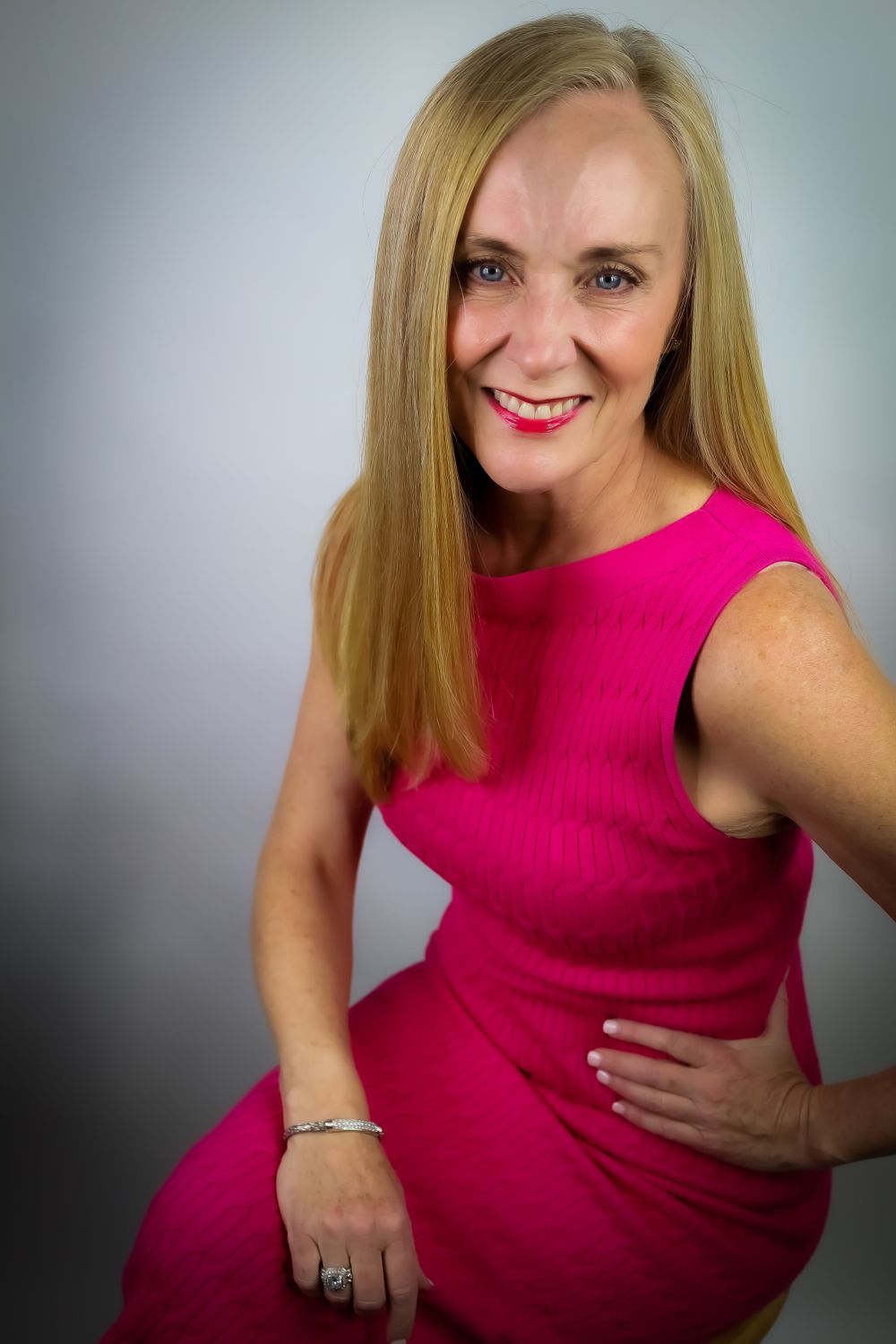 Portrait of person in vibrant pink sleeveless dress against grey studio background.