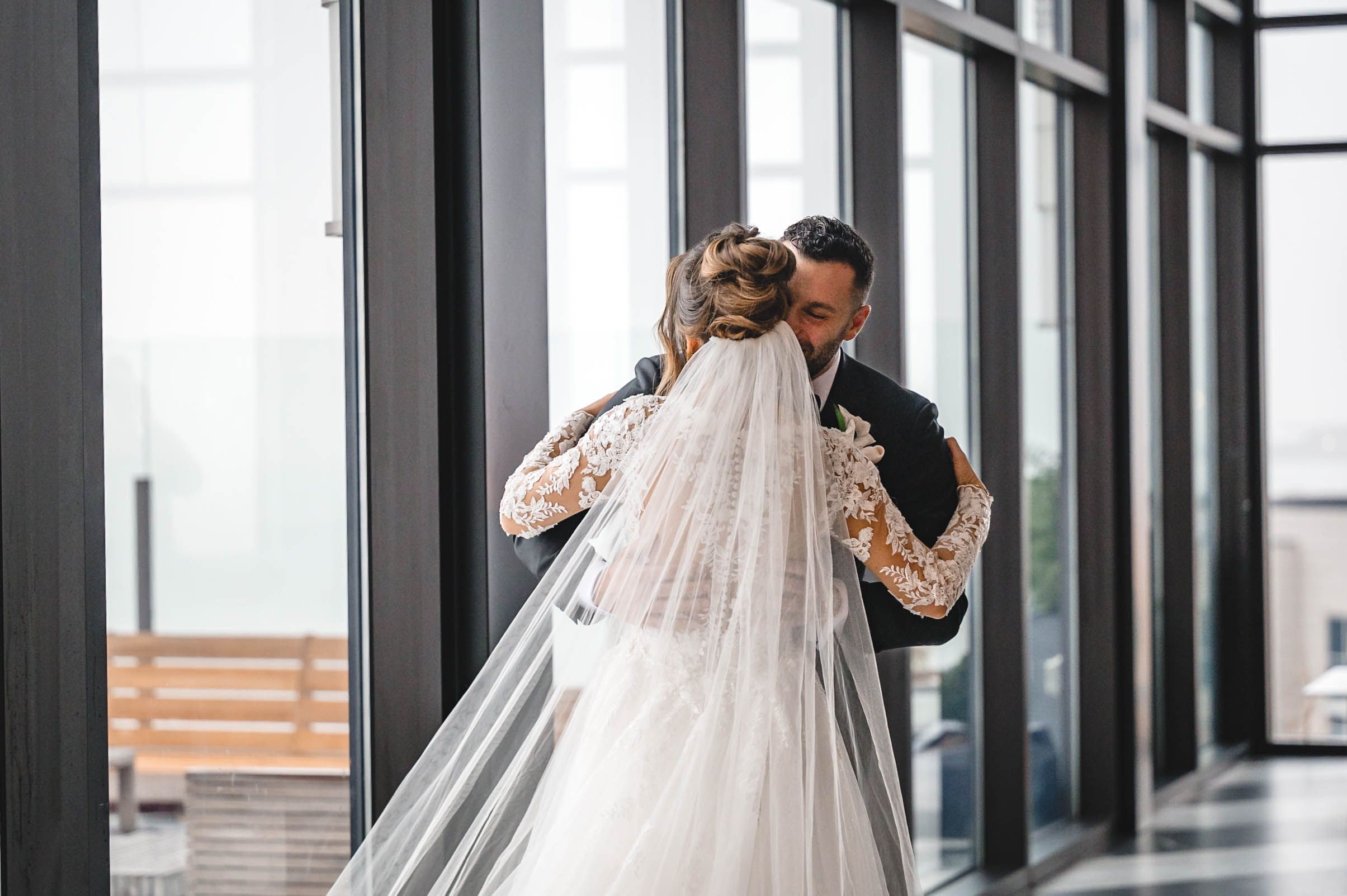 Wedding couple embracing in an intimate moment by large windows with natural light.