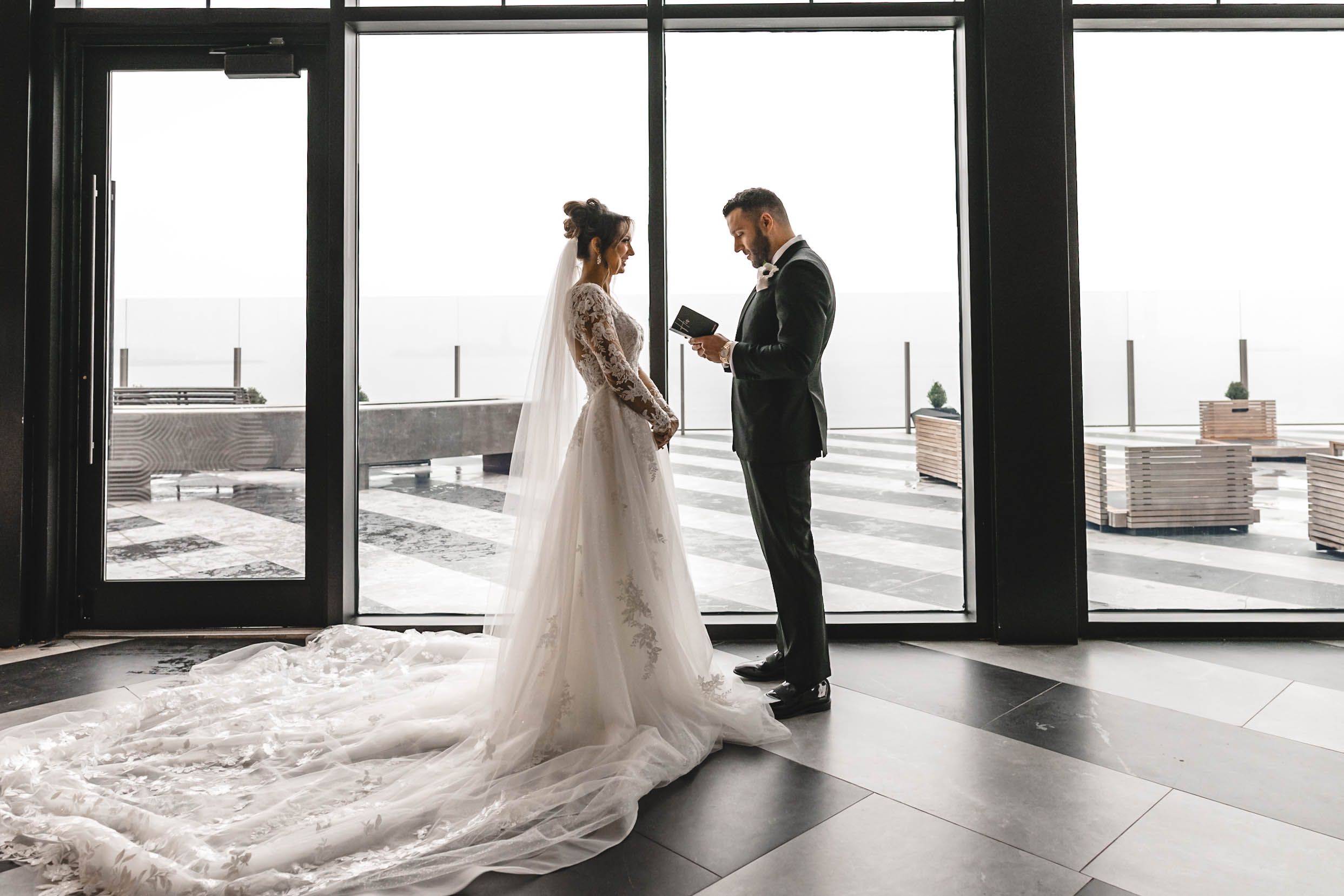 Bride and groom share an intimate first look moment in a modern venue with floor-to-ceiling windows.
