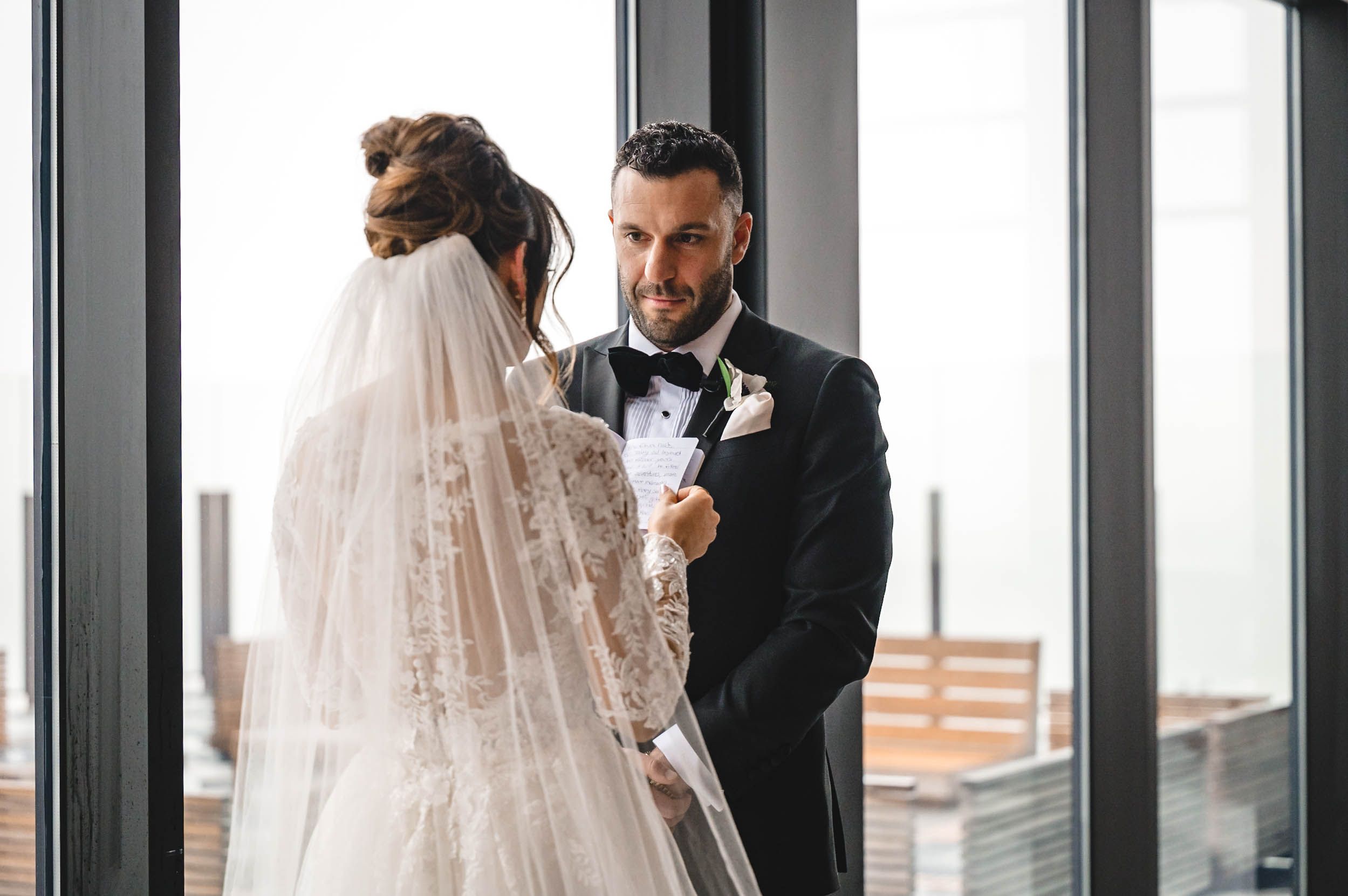Elegant couple shares their first look in front of large windows with natural light streaming in.