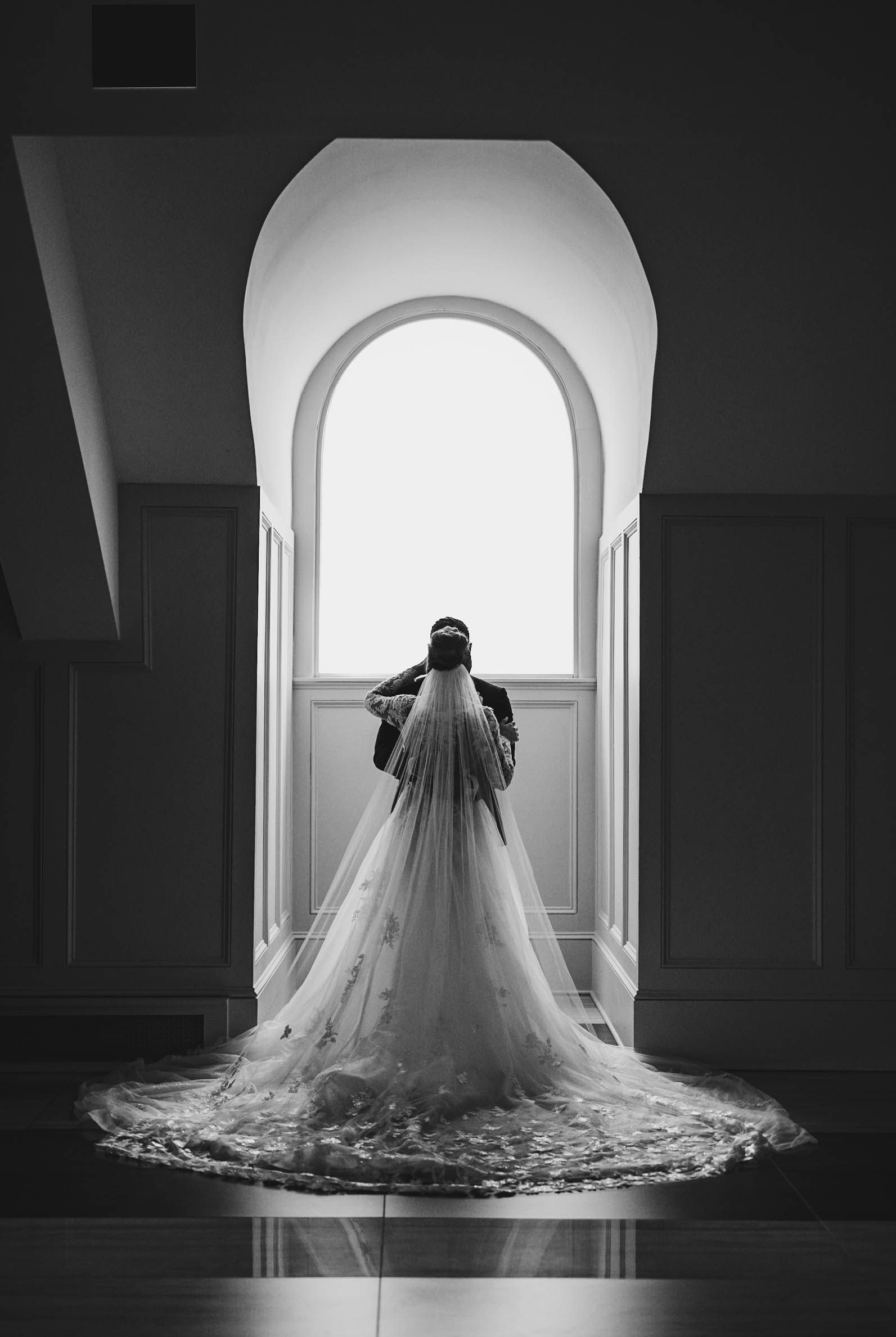 Dramatic black and white silhouette of bride with cathedral veil in arched doorway.