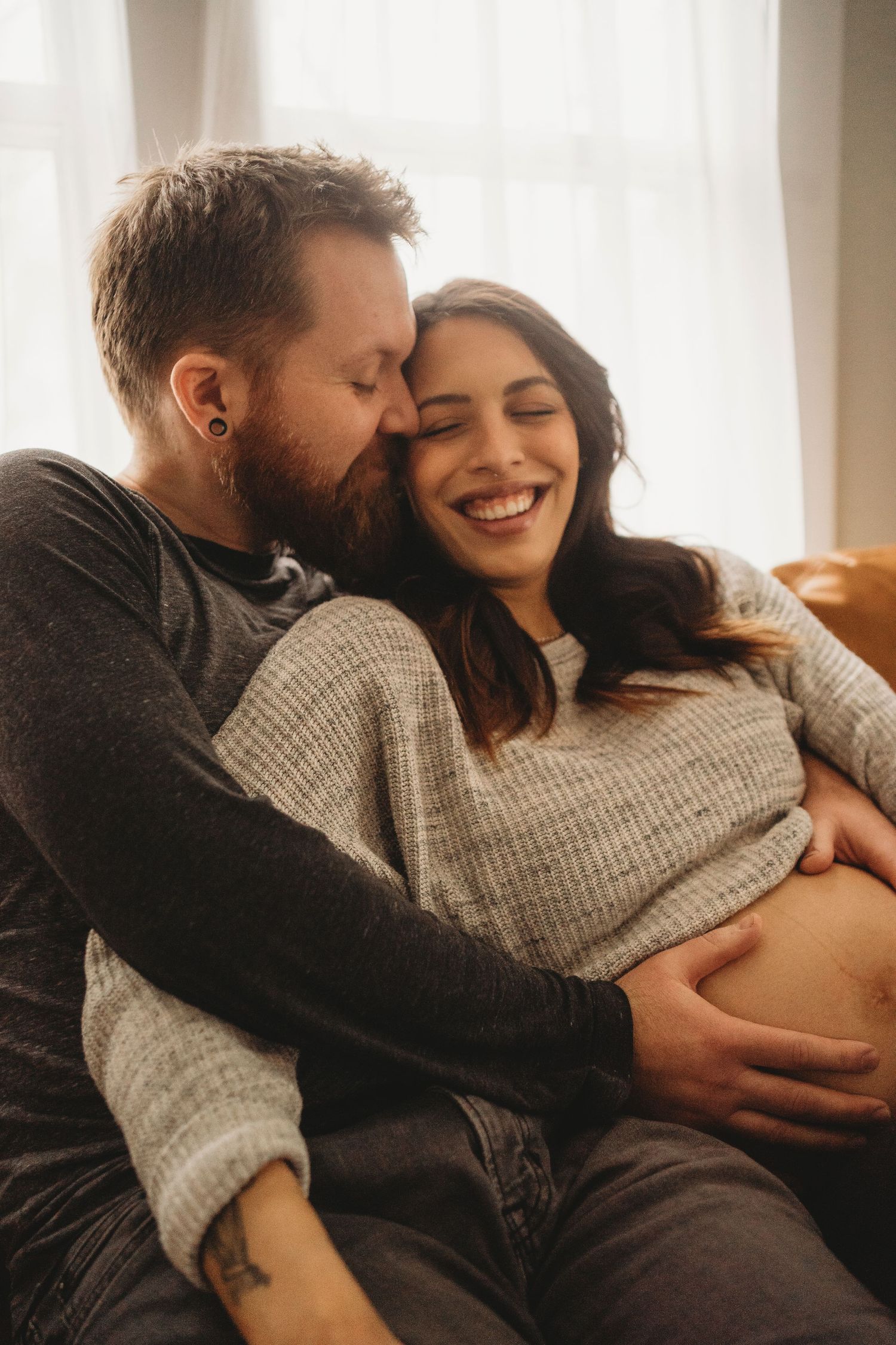 A loving couple embraces on their couch while sharing a joyful moment together.