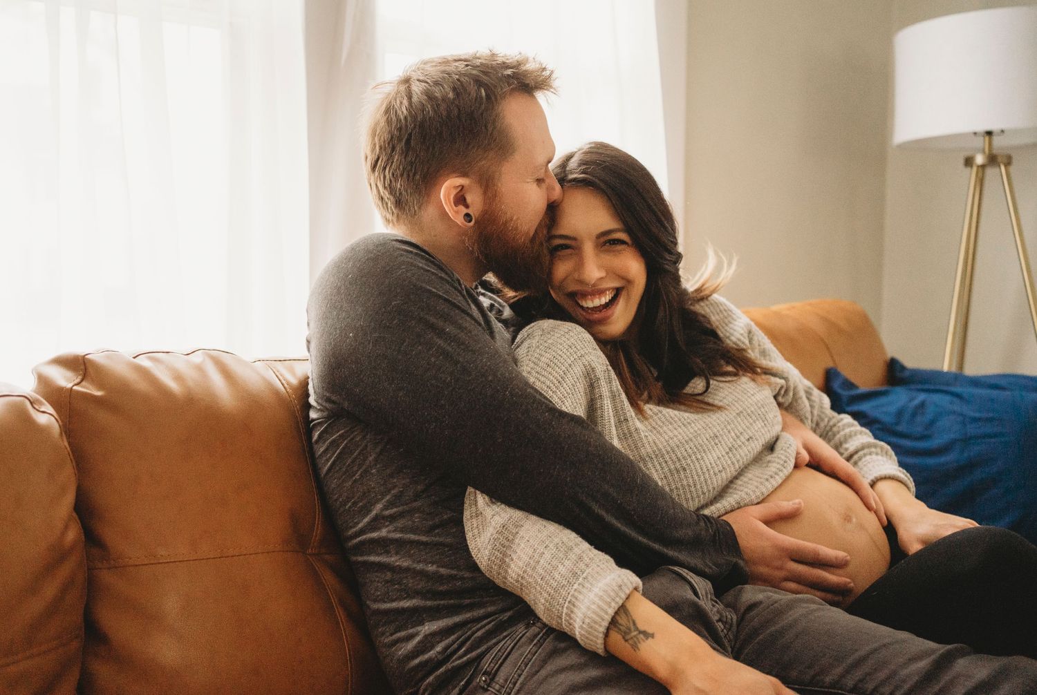 A couple shares an intimate moment while relaxing together on a brown leather couch in their living room.