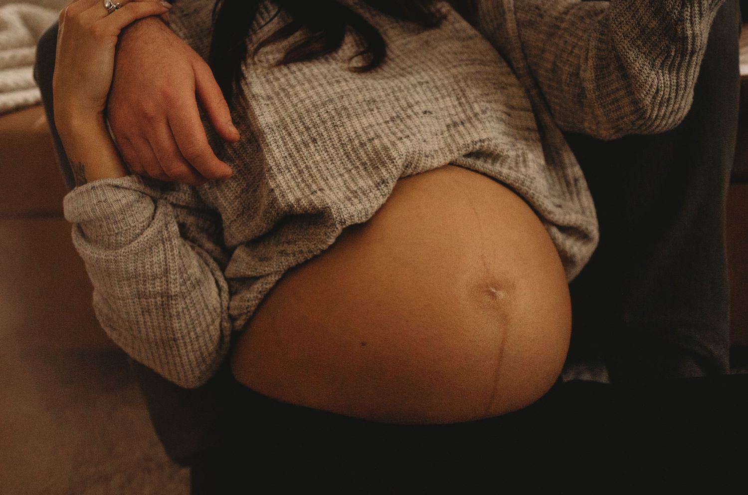 A close-up view of a pregnant belly with hands resting gently on it.
