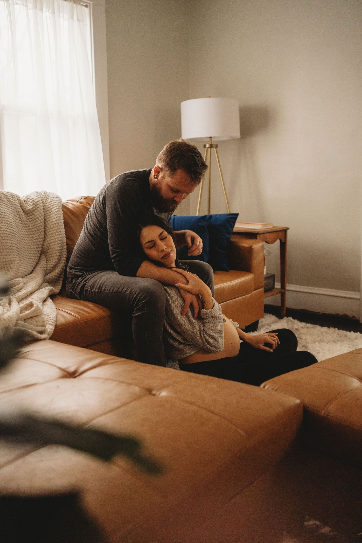 A couple relaxes together on their brown leather couch in a cozy living room setting.