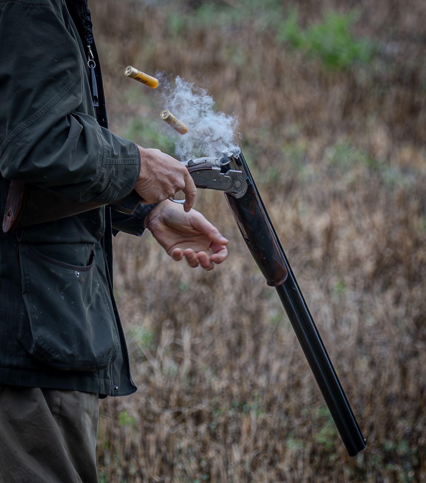 Close-up of hands loading ammunition into a black shotgun outdoors.