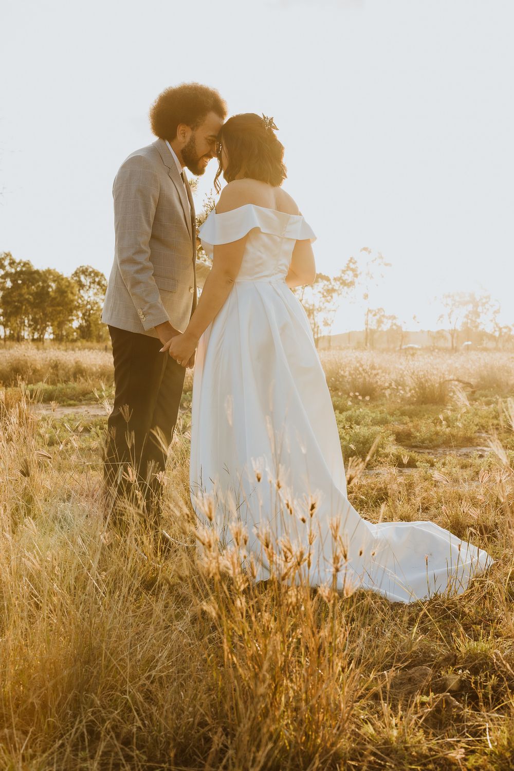 Romantic bride and groom sharing a kiss at golden hour in a dry grass field, bride in flowing white gown.
