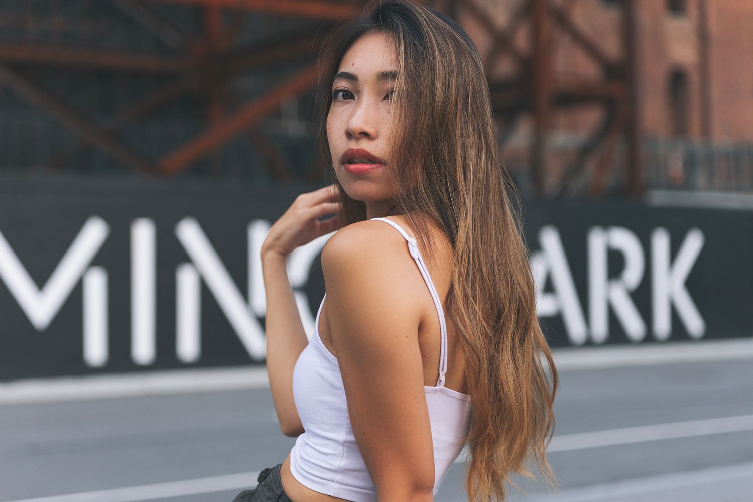 Woman in white tank top posing near urban wall with text.