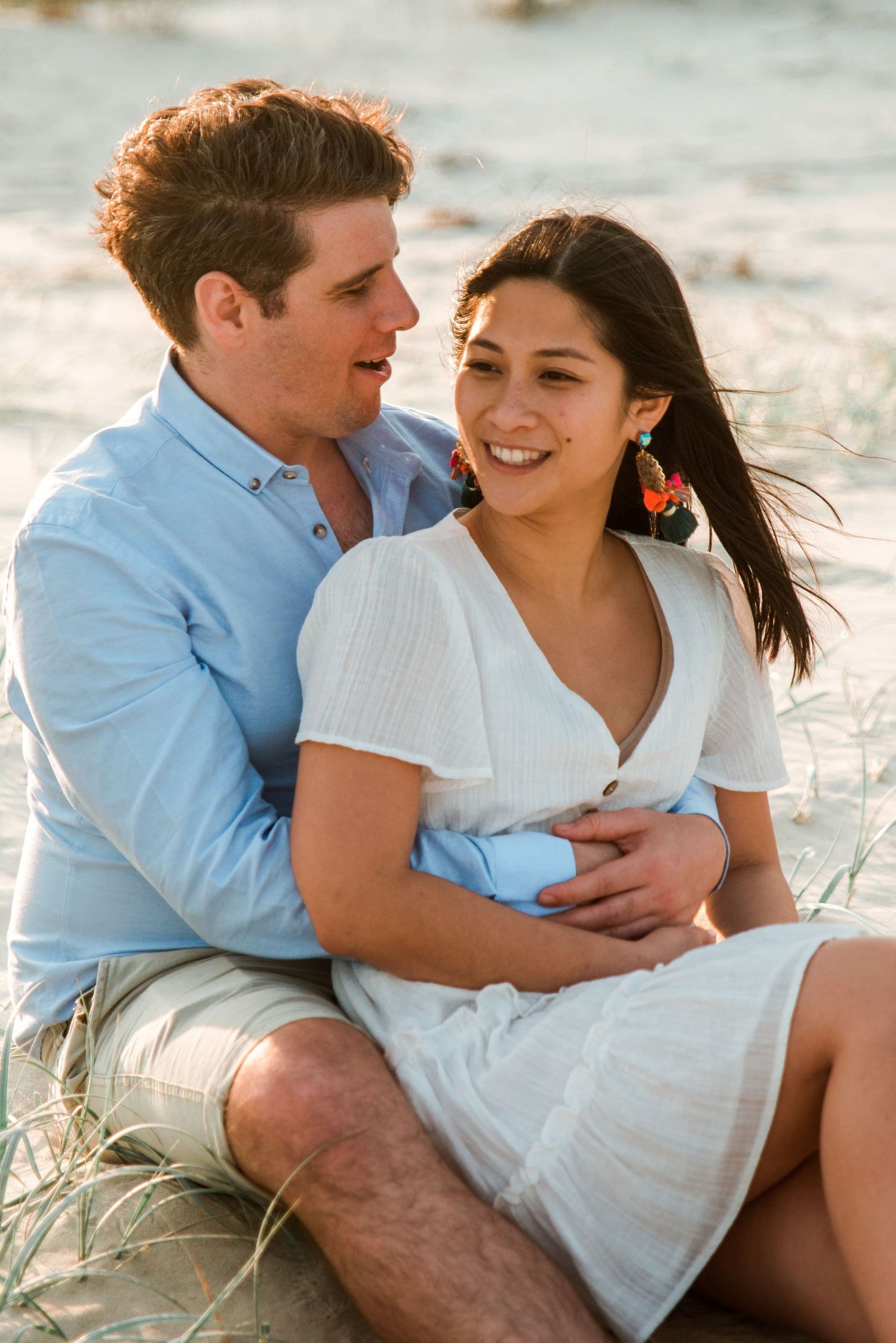 Couple sharing intimate moment while sitting on beach with warm sunset lighting.