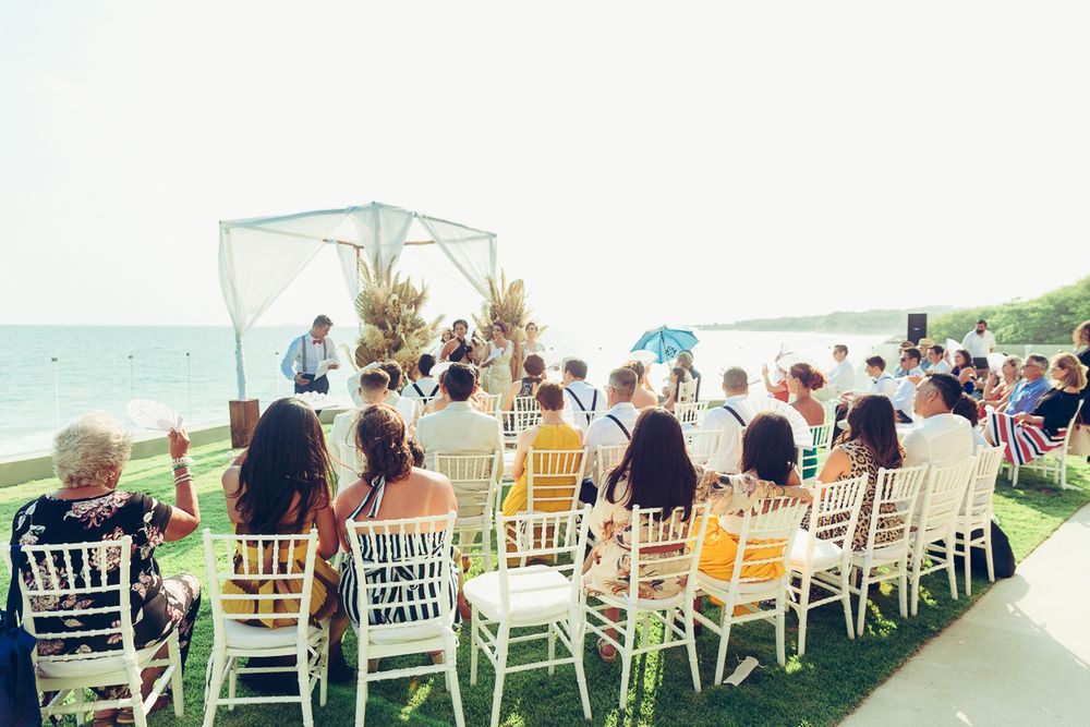 An outdoor wedding ceremony setup with white chairs and oceanfront views under a sheer canopy.