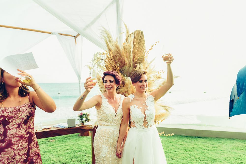 Wedding celebration on a lawn with people in white dresses raising glasses in celebration.