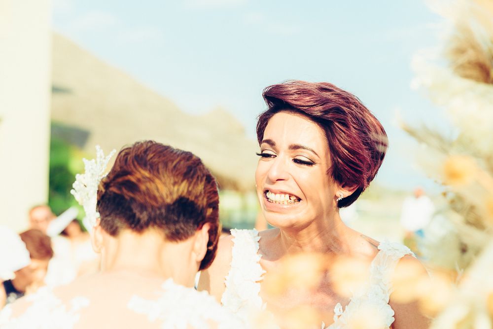 A candid moment between two people in elegant white lace dresses during an outdoor celebration.