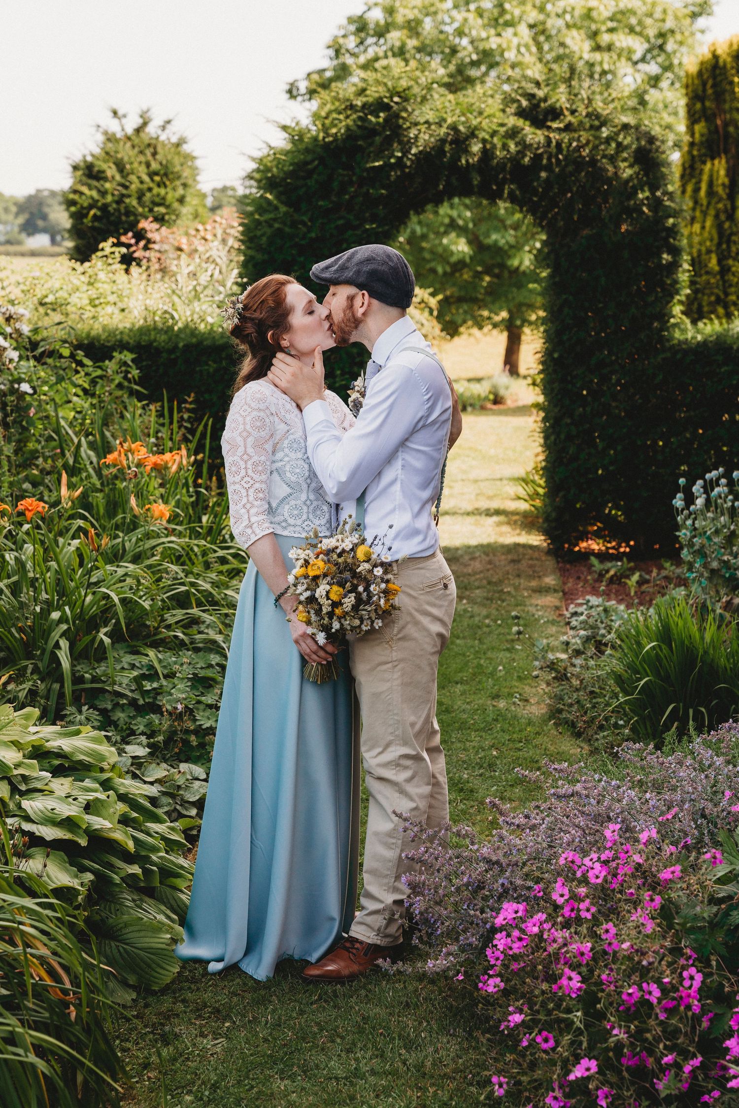 Garden wedding portraits with colorful summer flowers and stone wall backdrop.