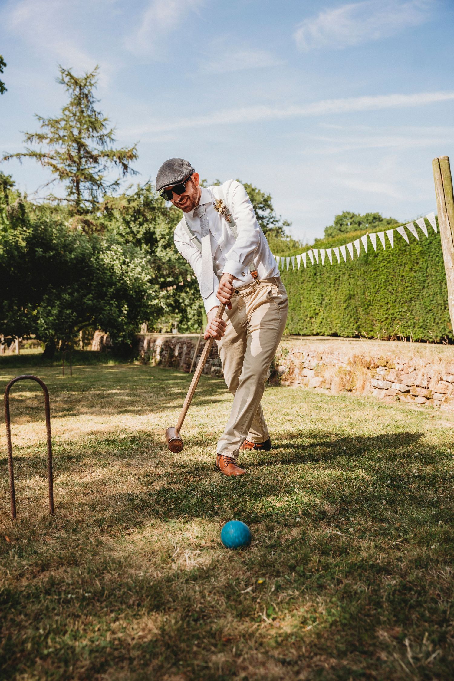 Wedding guests playing croquet on sunny lawn during outdoor reception.