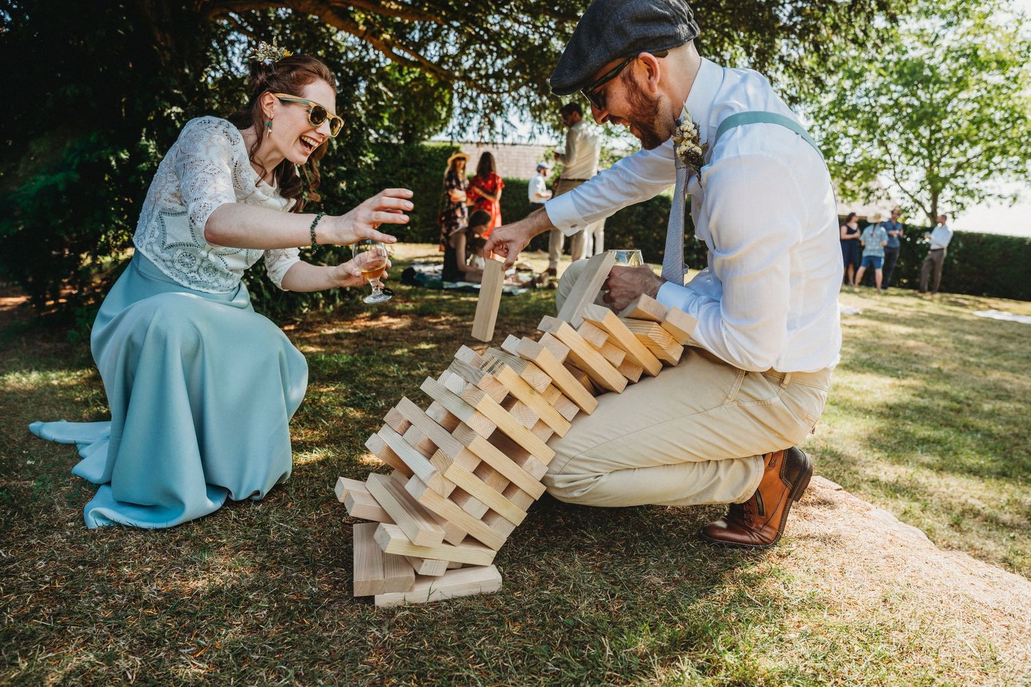 Wedding guests playing outdoor games with wooden pallets in garden setting.
