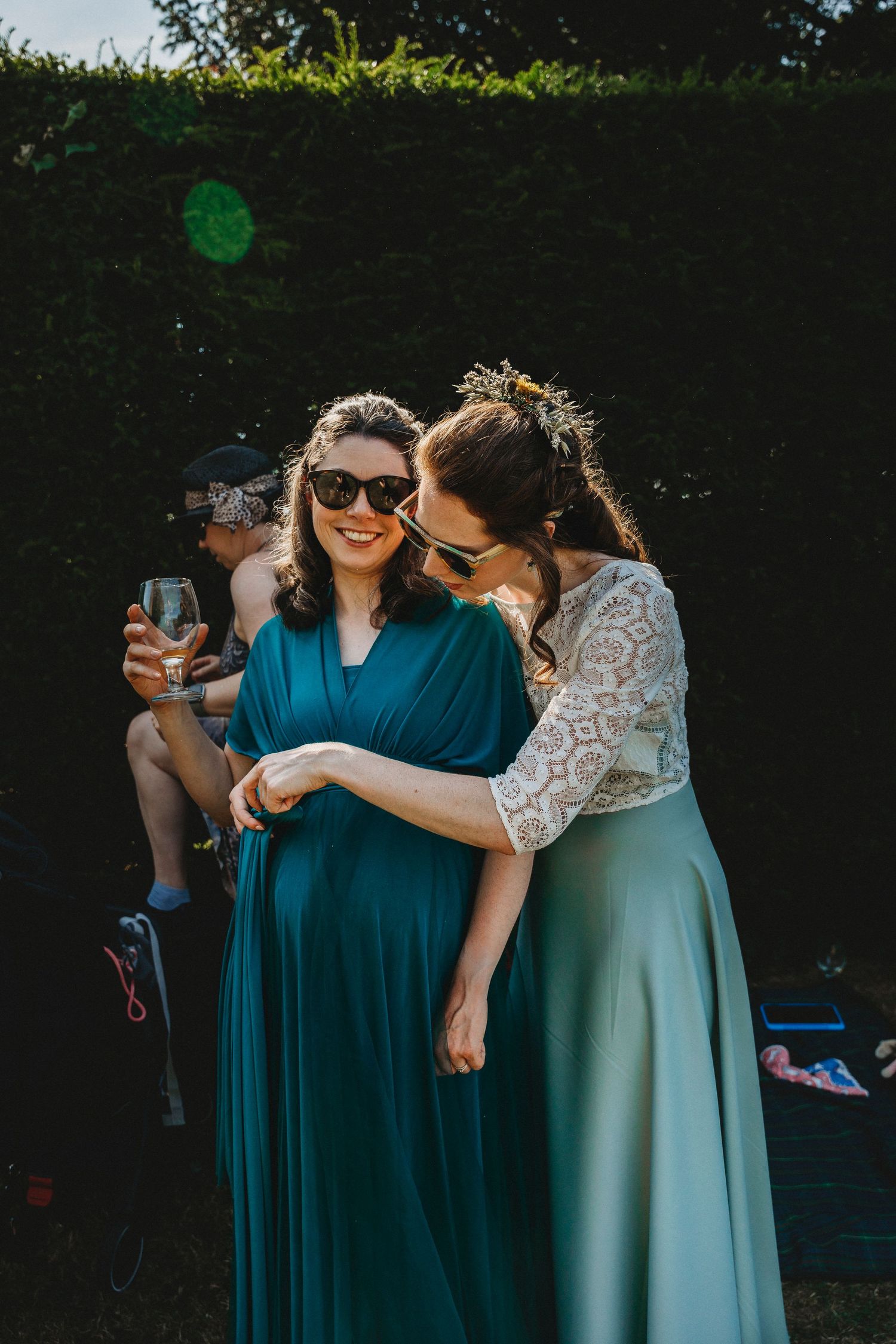 Wedding guests in teal and dark blue dresses sharing laughs at outdoor reception.