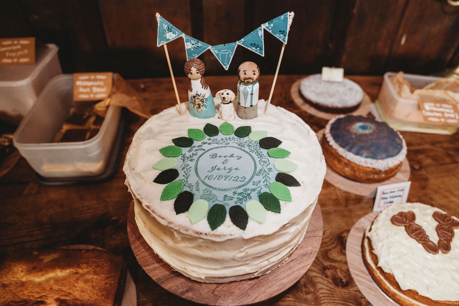 Wedding cake display featuring blue bunting and decorative toppers on wooden table.