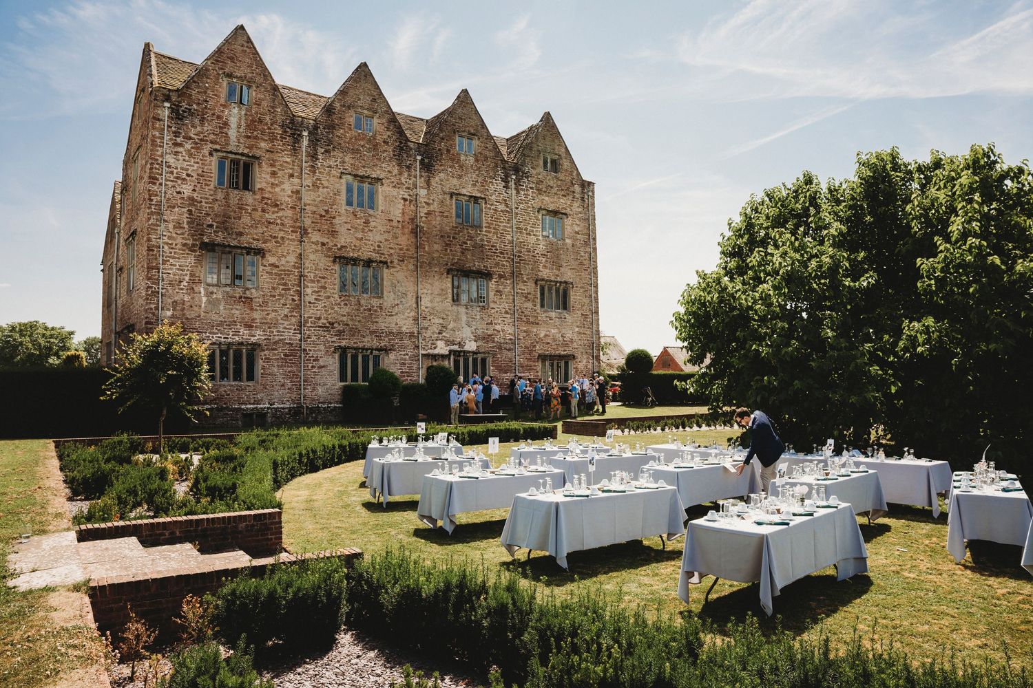 Outdoor wedding reception setup with white tables against stone castle backdrop.