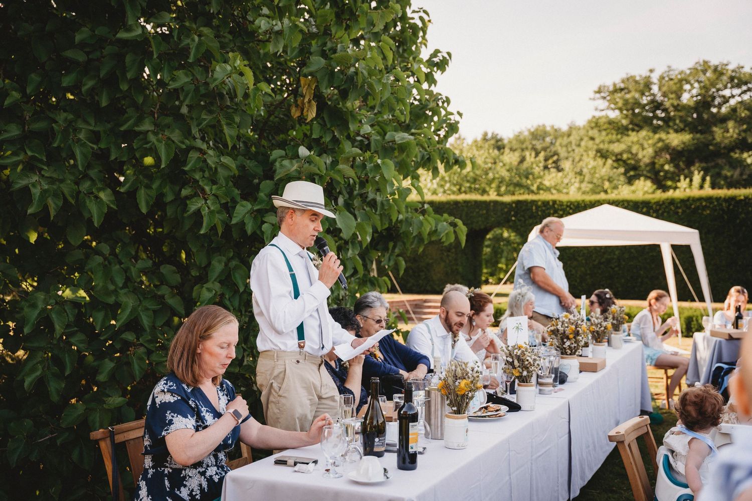 Guests enjoying dinner at elegant outdoor wedding reception with white tablecloths.