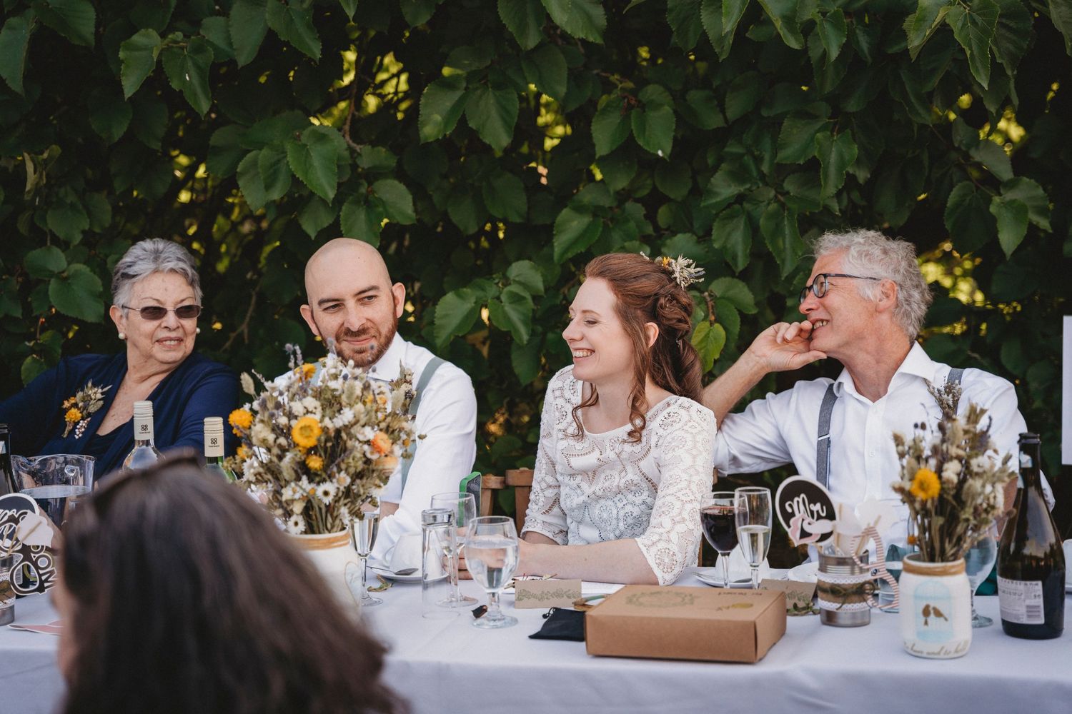 Wedding guests enjoying an outdoor reception dinner at elegantly set tables under green foliage.