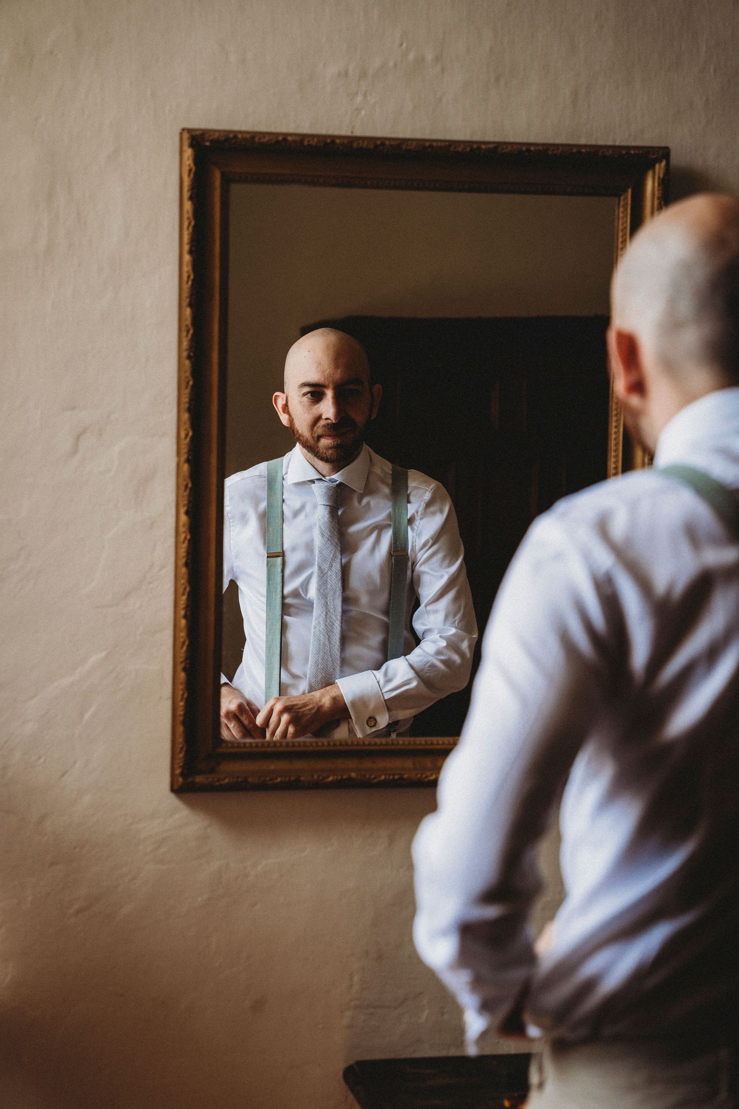 Person in formal attire looking in mirror while getting dressed.