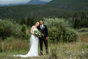 A wedding portrait set against a scenic mountain landscape with lush greenery.