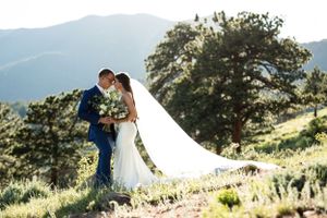 A couple embraces on a hillside with dramatic mountain views and flowing white veil.