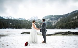 A winter wedding couple holds hands in front of a snow-covered mountain landscape.